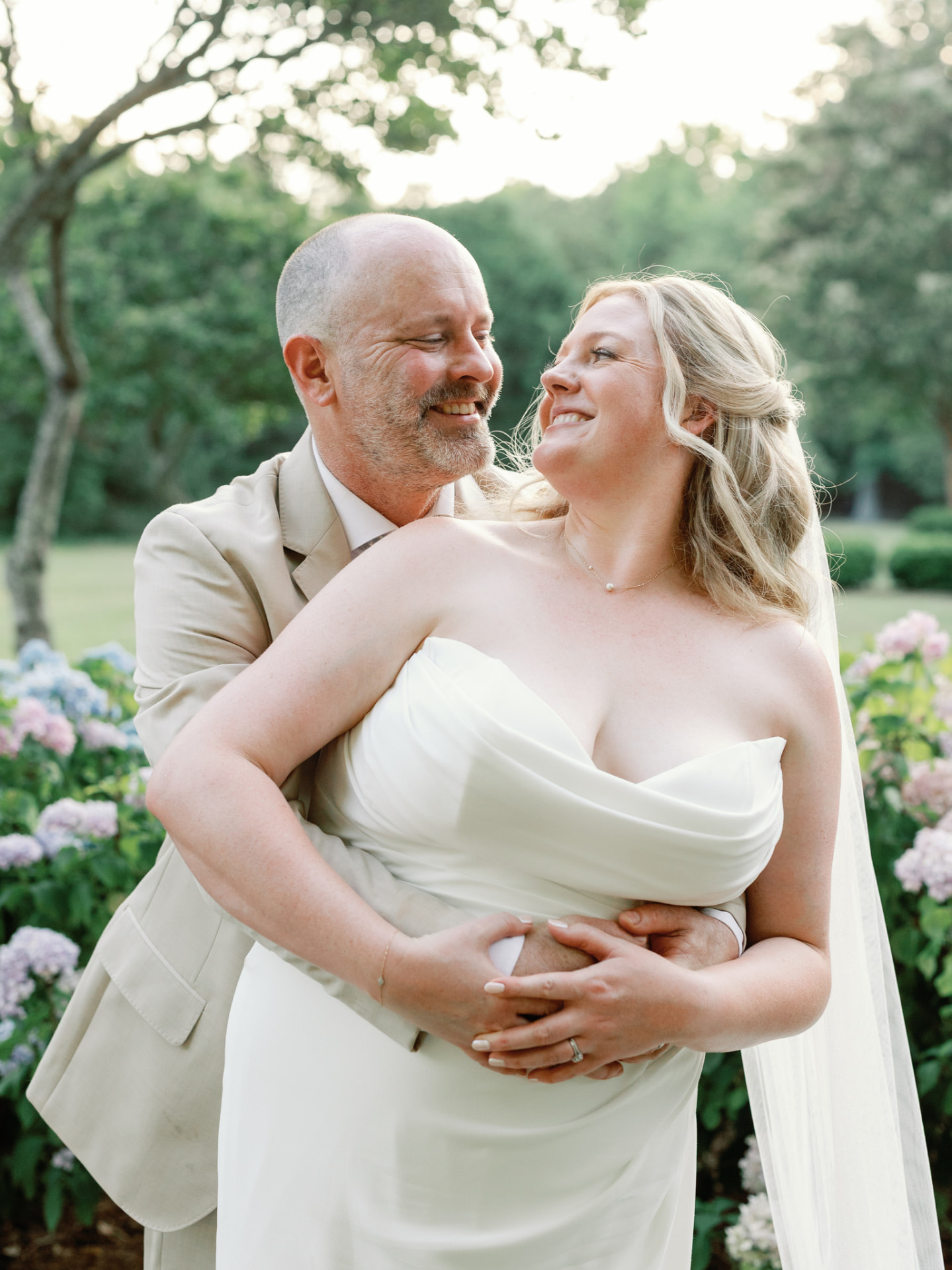 Couple laughing among hydrangeas, veil catching the light